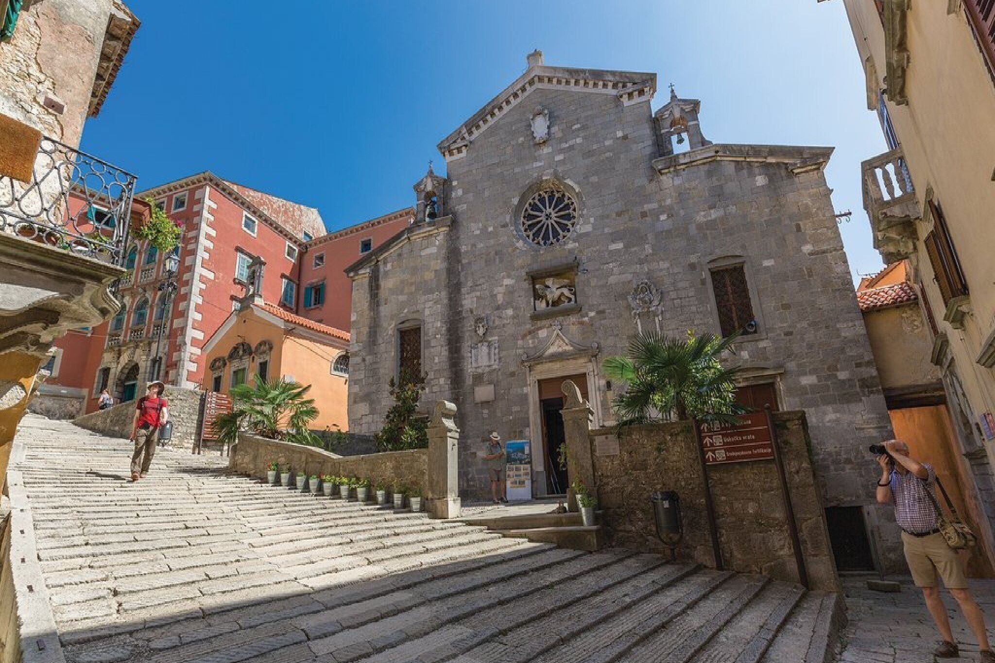 A historic stone building with a clock tower, a staircase leading to the entrance, and a sign indicating a tourist information center.