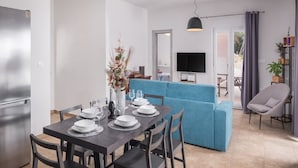 Un salon moderne avec un canapé bleu, une table à manger pour quatre personnes et un téléviseur à écran plat fixé au mur.