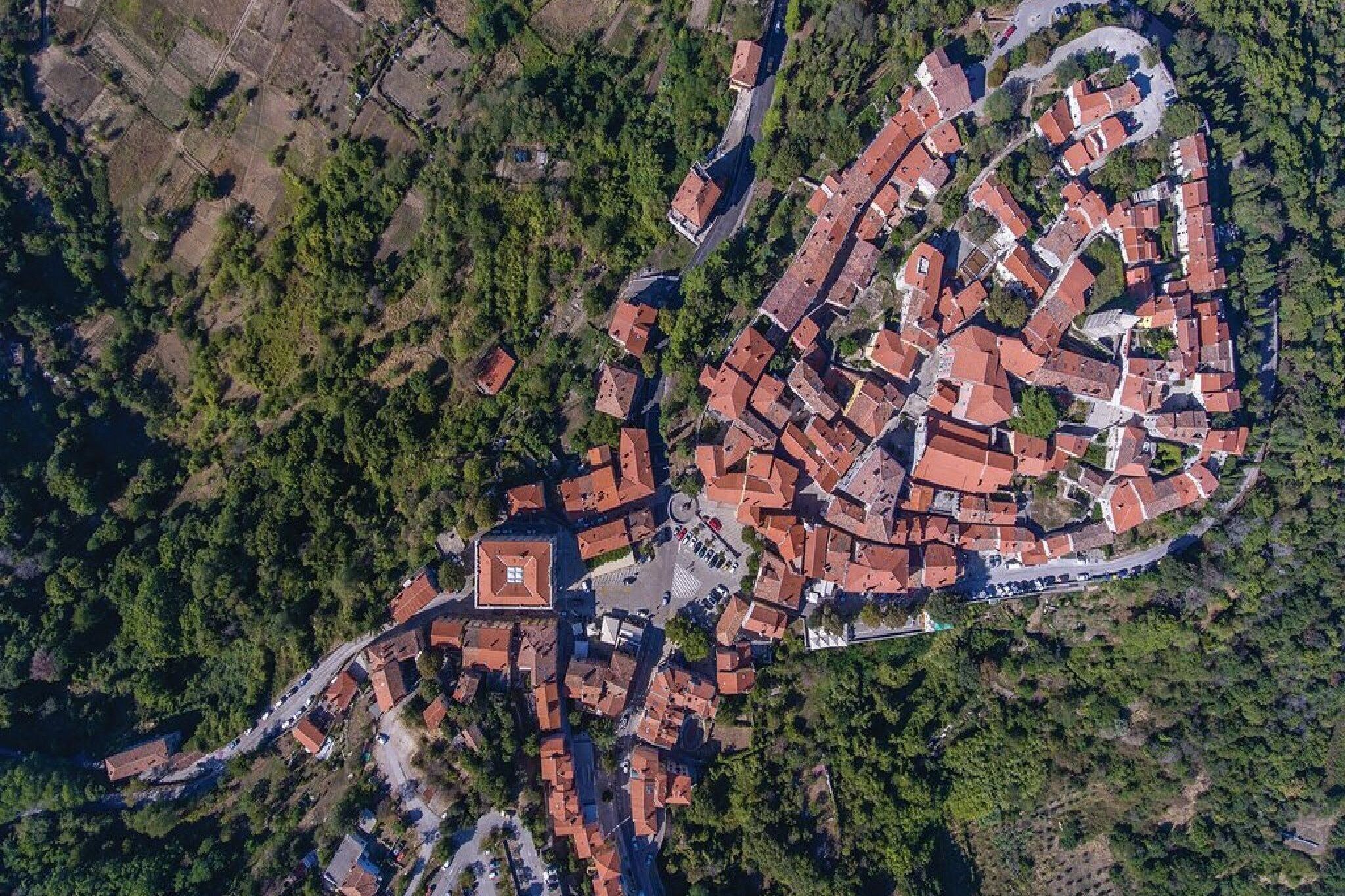 Vista aérea de uma cidade com uma praça central, rodeada por edifícios com telhados vermelhos e vegetação densa na periferia.