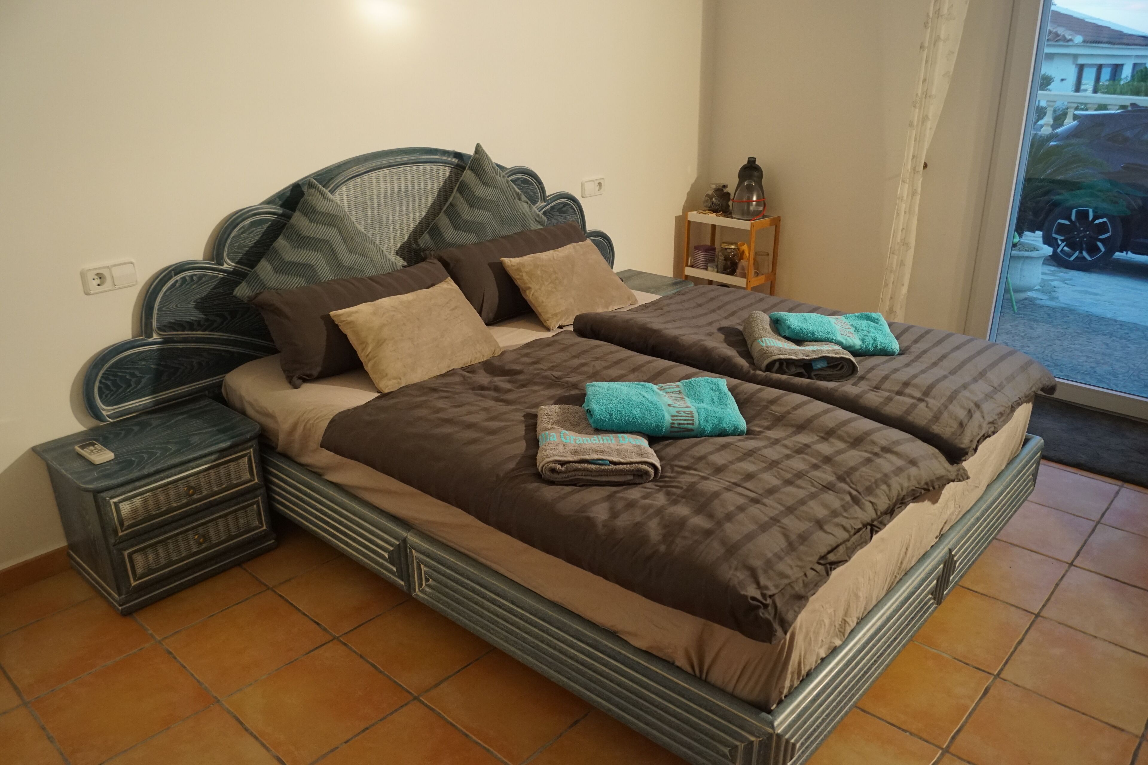 Un lit double avec une tête de lit, deux tables de chevet et une petite étagère ornée d’objets décoratifs.
