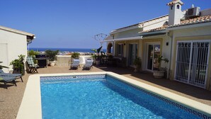 Une piscine avec un bord carrelé, des chaises longues et des plantes en pot.