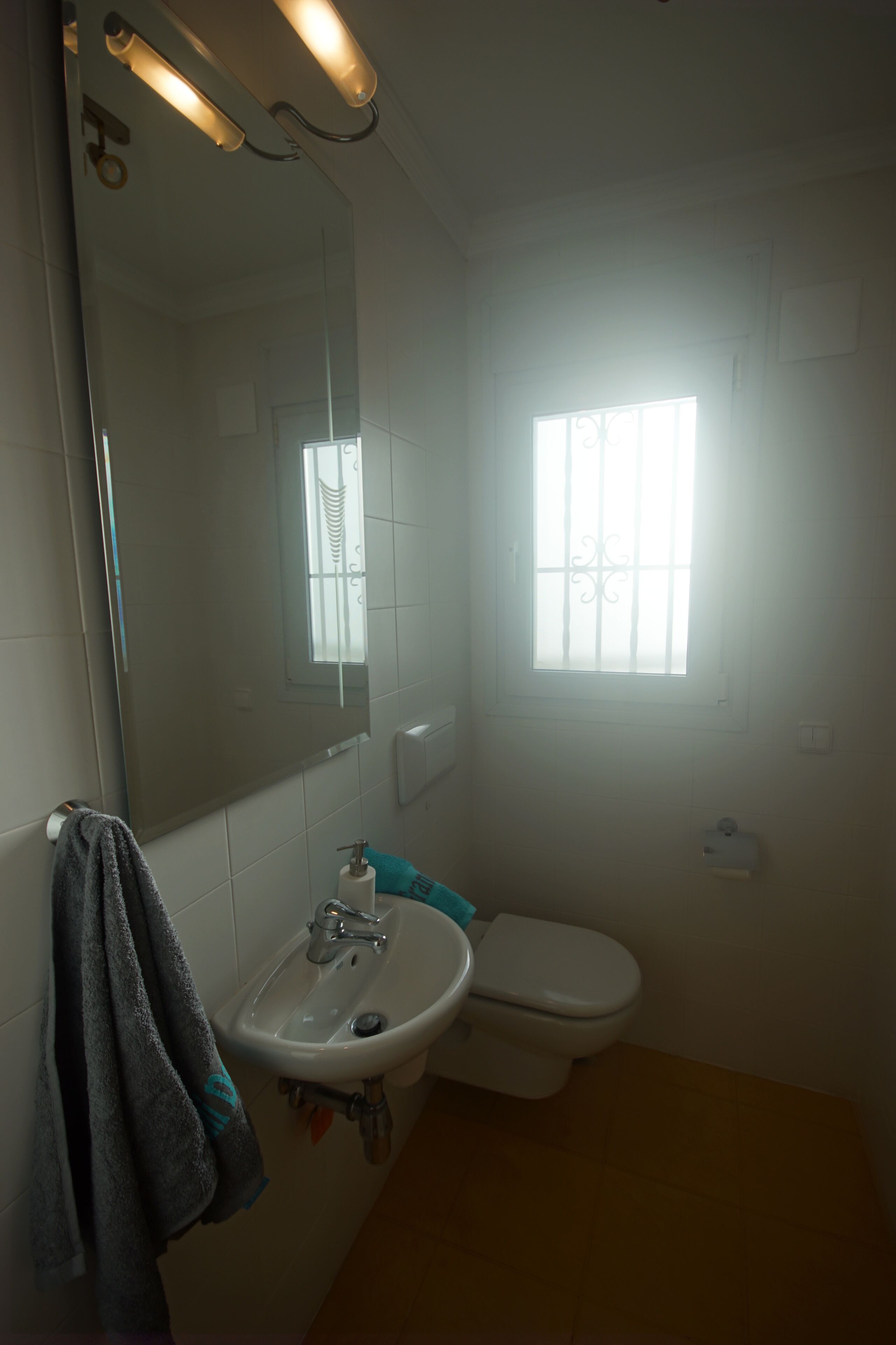 Une salle de bain avec un lavabo, des toilettes et une fenêtre avec des barreaux.