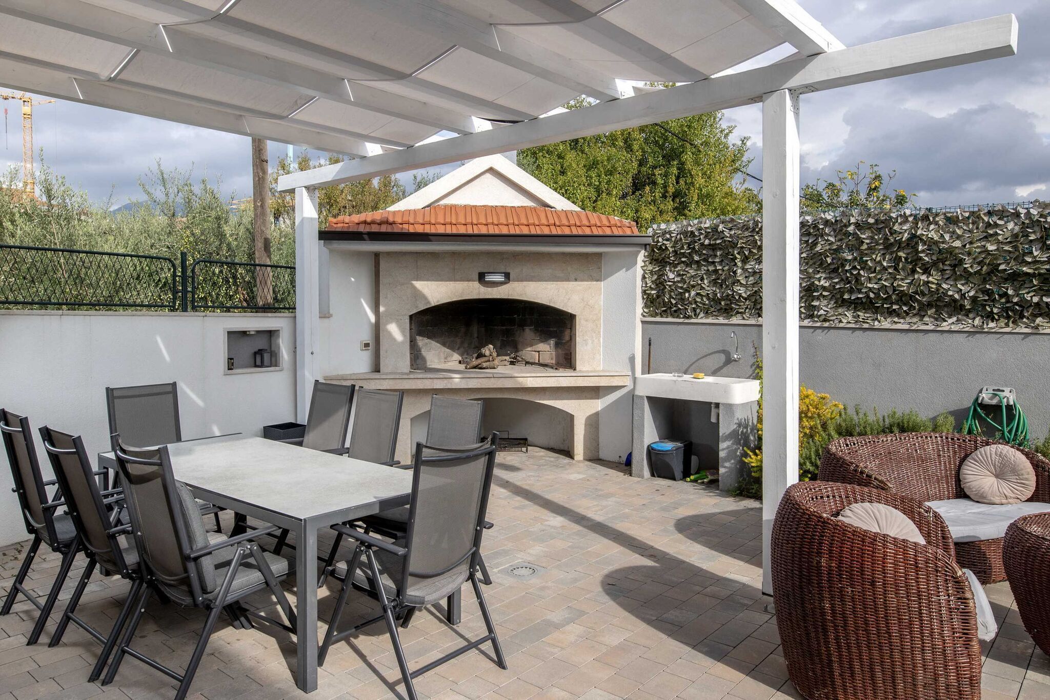 Une terrasse extérieure dotée d’un four à pizza intégré, d’une table avec des chaises et de mobilier en osier.