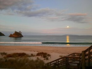 A beach with a wooden walkway leading to the water, a rocky outcrop in the distance, and a calm sea reflecting the sky.