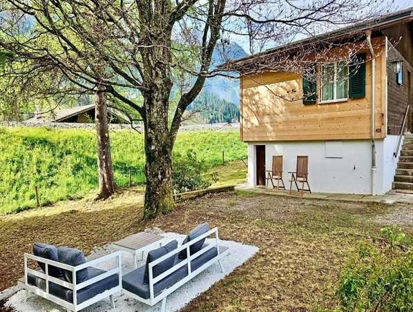 A wooden cabin with a balcony, two chairs, and a table outside. - Cosy Chalet With Garden (Rougemont)