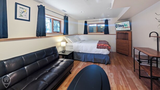 Ein Hotelzimmer mit einem Bett, einem schwarzen Ledersofa, einem kleinen Tisch mit Lampe, einem hölzernen Schminktisch und einem Fernseher an der Wand.