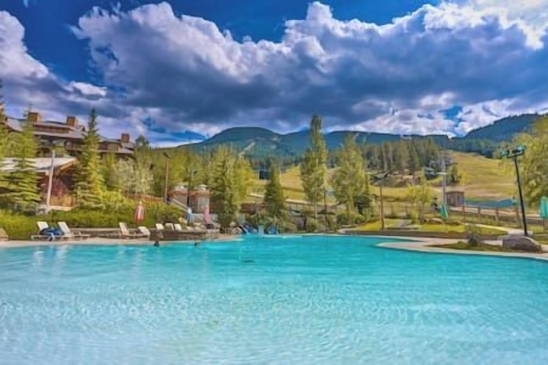 A clear blue pool with lounge chairs, surrounded by trees and a mountainous landscape.