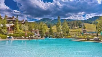 A clear blue pool with lounge chairs, surrounded by trees and a mountainous landscape.