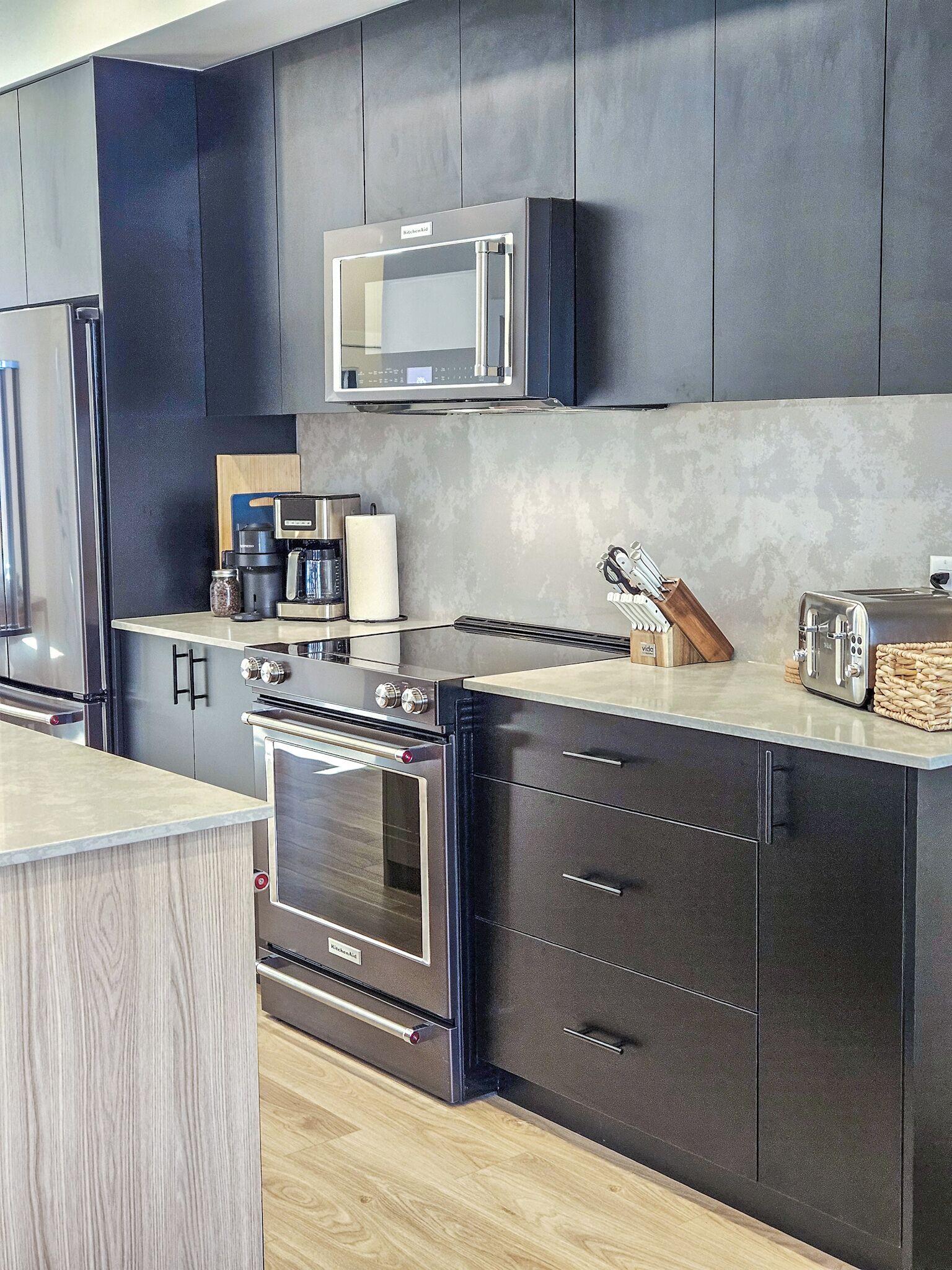 A modern kitchen with dark cabinetry, a built-in microwave, a coffee maker, and a toaster.