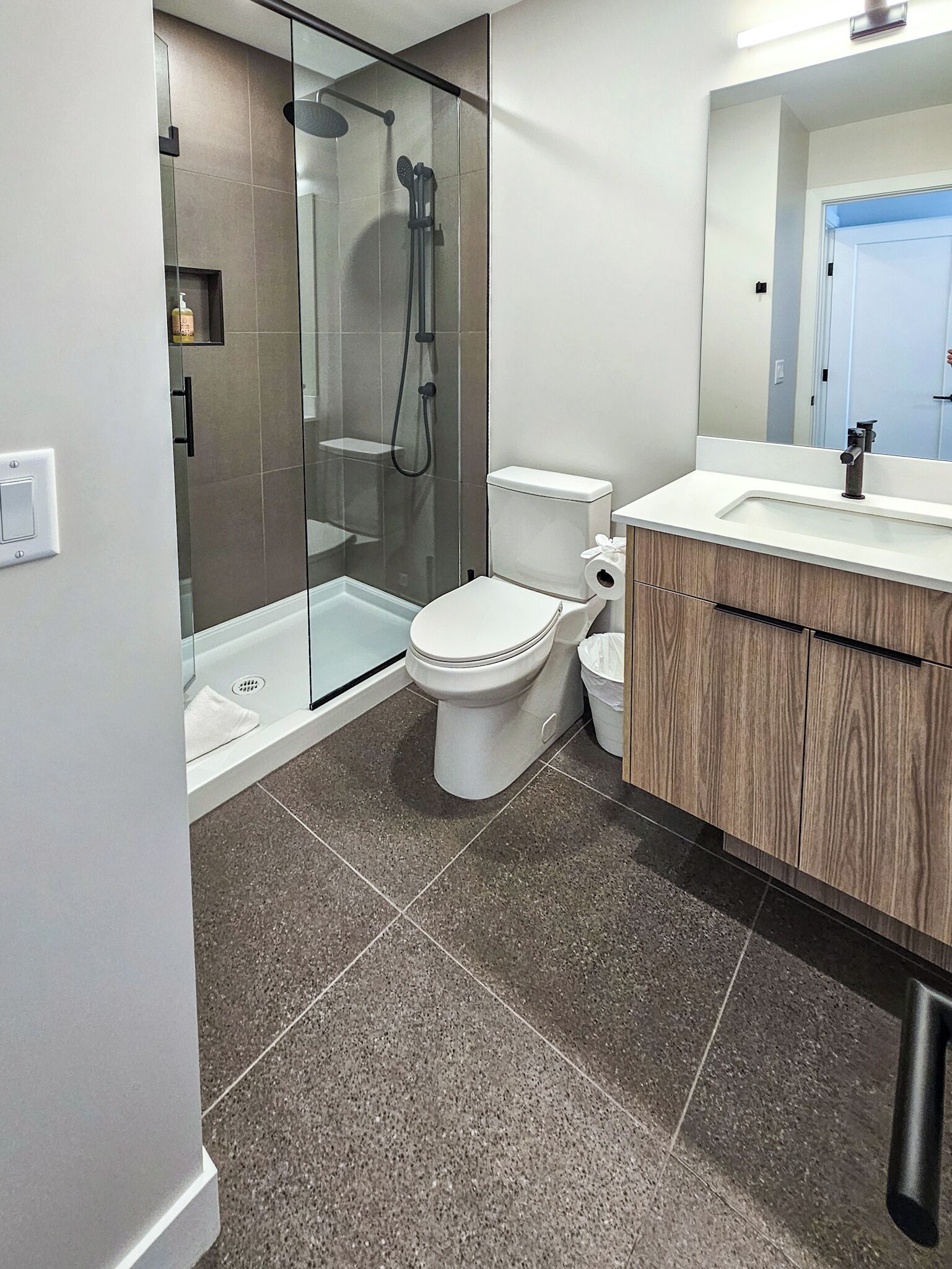 Une salle de bain moderne avec une douche à parois de verre, des toilettes blanches et un meuble-lavabo en bois avec un évier.