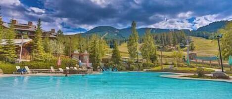 Une piscine d’un bleu éclatant, bordée de chaises longues, entourée d’arbres et avec une chaîne de montagnes en toile de fond.