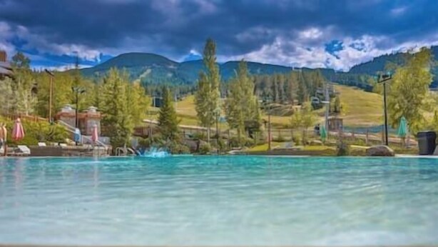 A swimming pool with a wooden deck in the foreground, surrounded by trees and a mountainous landscape in the background. - Nordix Townhome / Private hot tub / New build (Panorama)