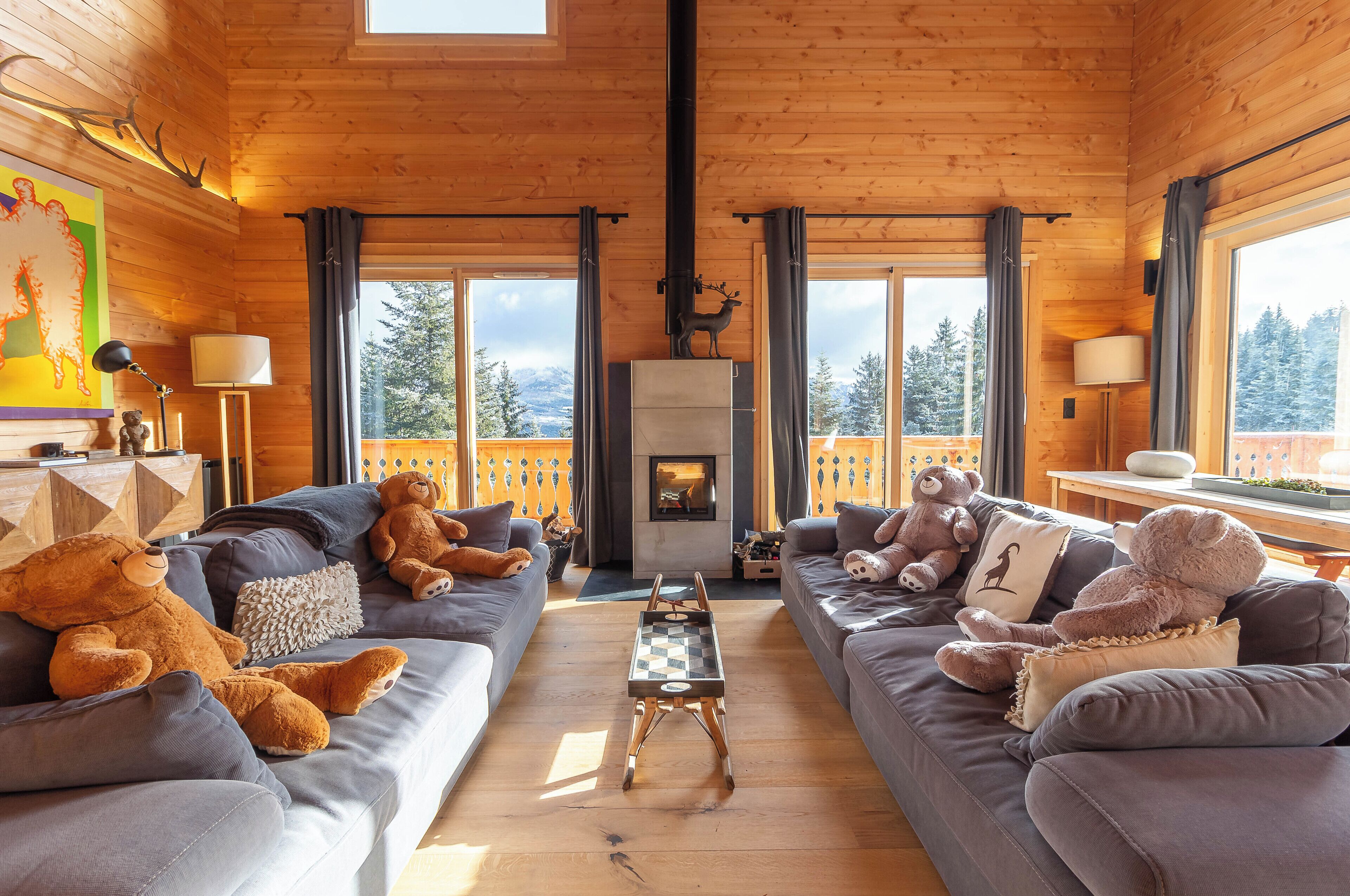 Interior acogedor de una cabaña con dos sofás, una chimenea y grandes ventanales con vistas al bosque.