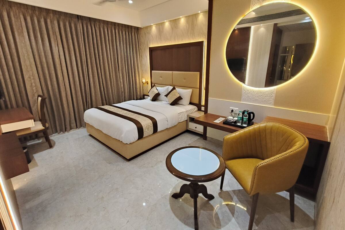 Una habitación de hotel con cama, mesita de noche, silla y un espejo redondo.