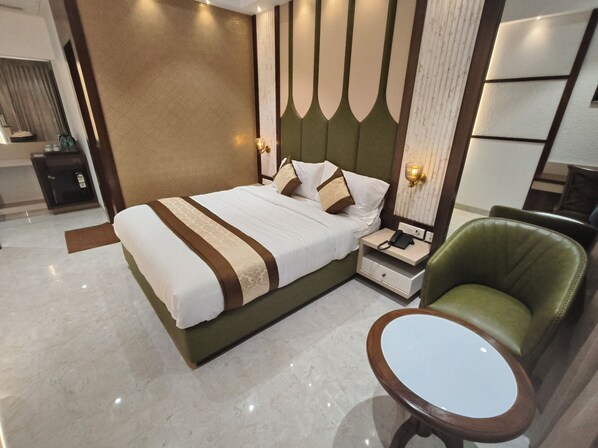 A modern hotel room with a large bed, a bedside table with a phone, a green armchair, and a small round table. - Hotel Sonesta Suites Thane (Thane)