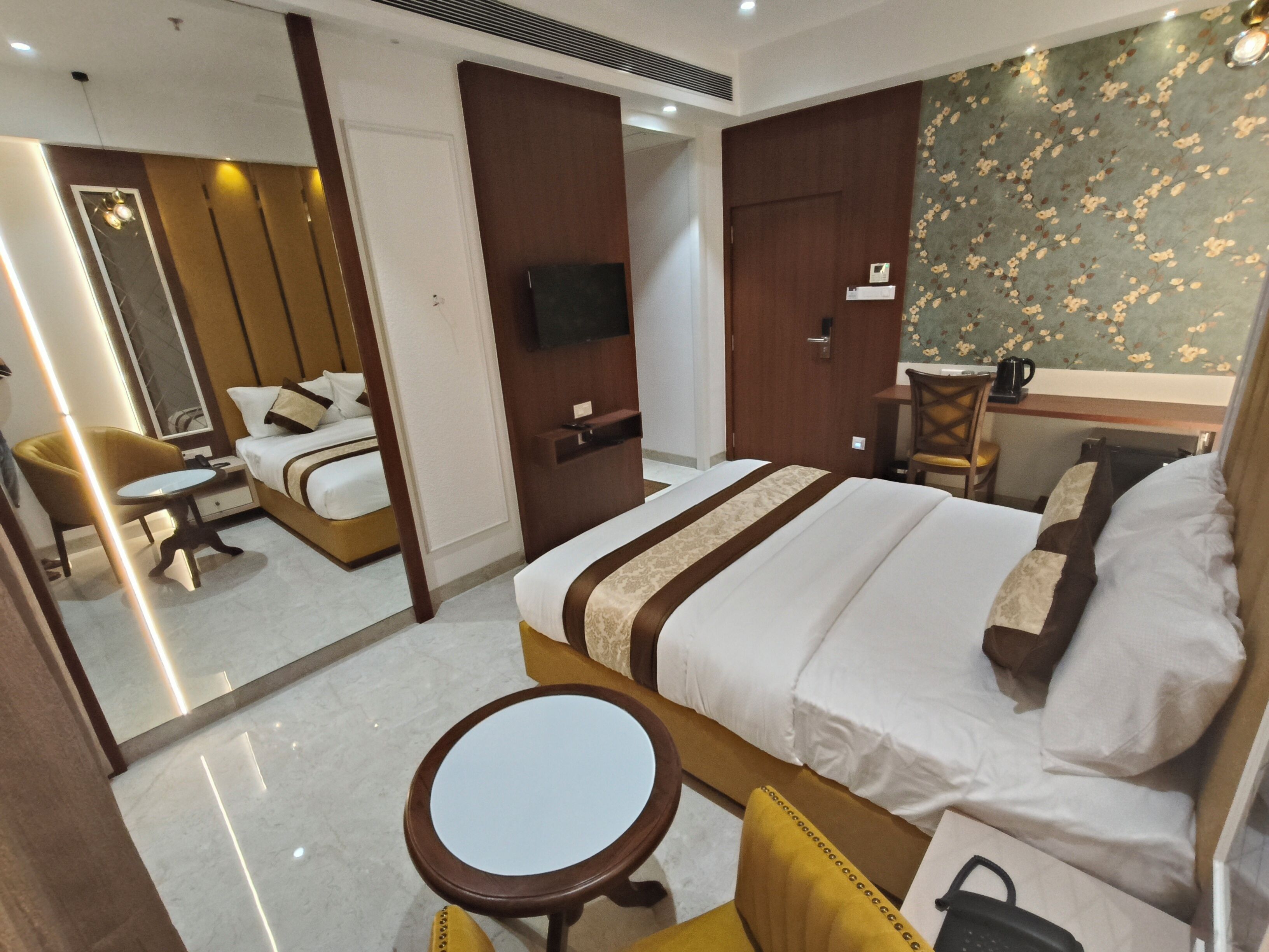 Habitación de hotel con cama, una mesita redonda, una silla, un escritorio con silla, televisor y espejo.
