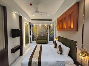 Een moderne hotelkamer met een groot bed, een televisie, een groene bank en een muurschildering van tropische planten.