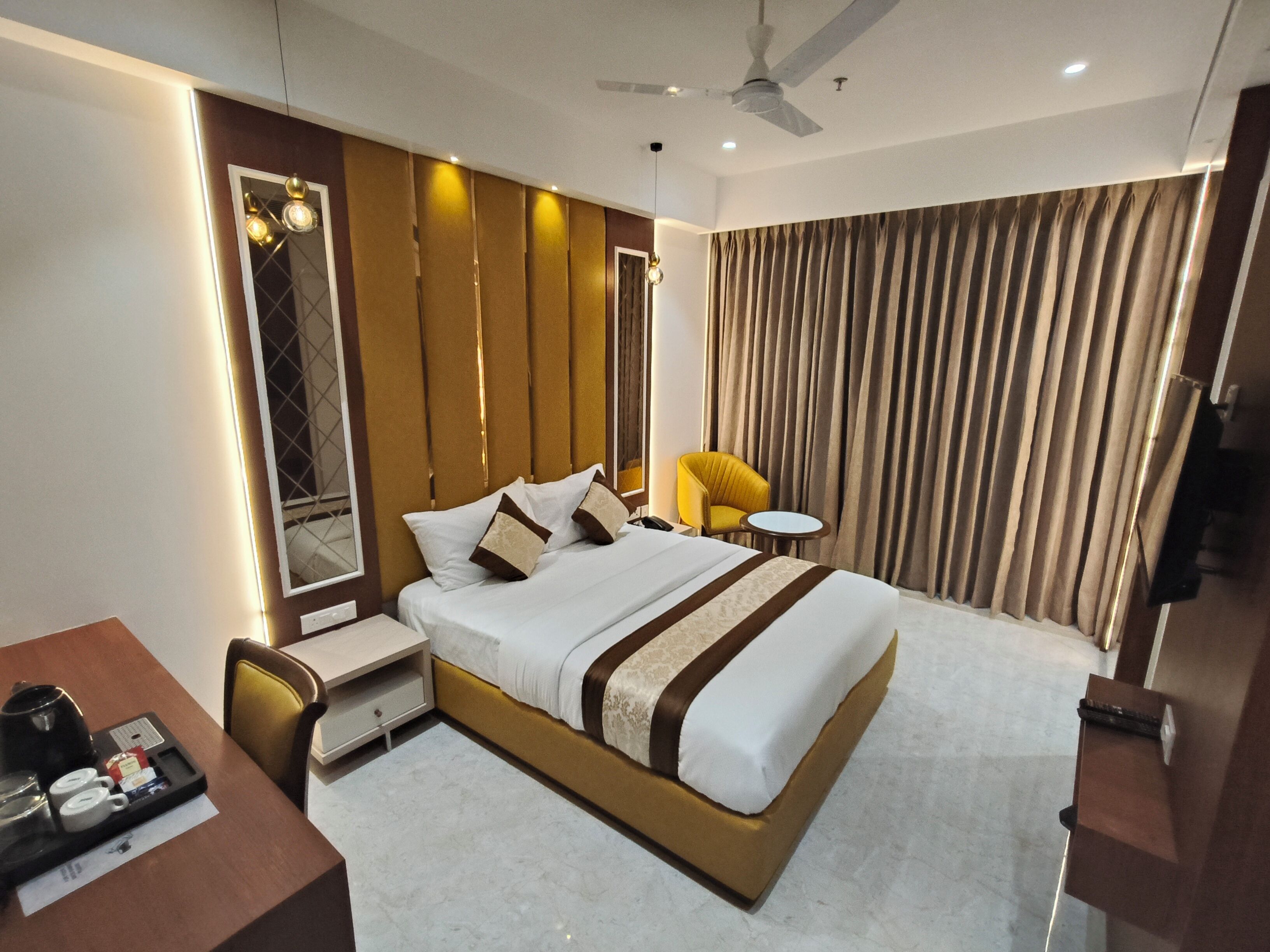 A modern hotel room with a large bed, bedside tables, a desk with a chair, a small round table, and a ceiling fan.