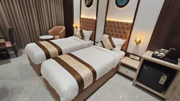 A hotel room with two beds, a small round table, a chair, a minibar, and decorative wall panels.