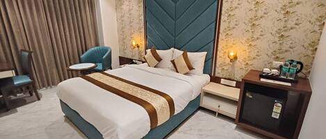 A hotel room with a large bed, a desk, a chair, a minibar, and a wall with floral wallpaper.