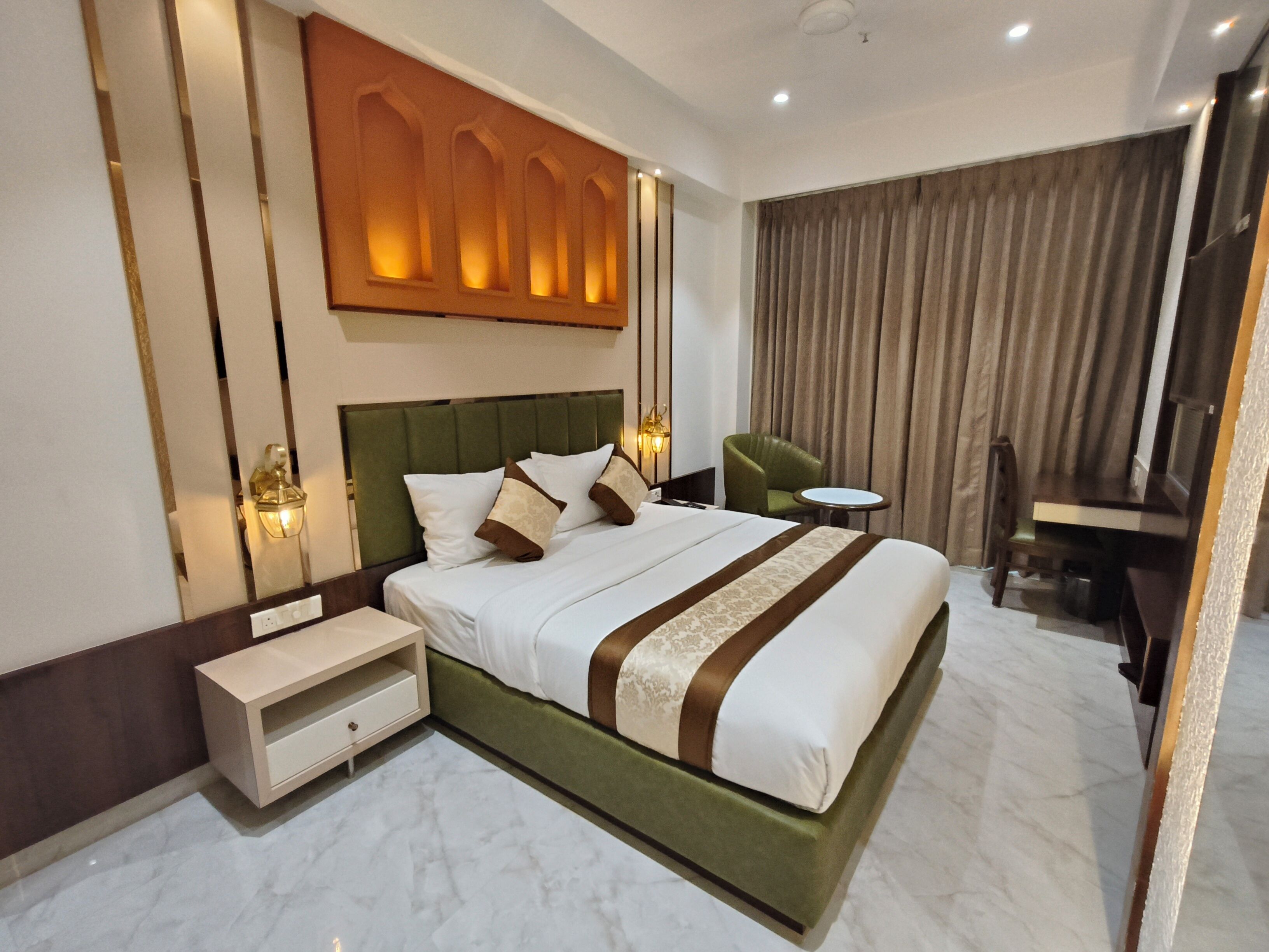 A hotel room with a large bed, a desk, a chair, and a nightstand.