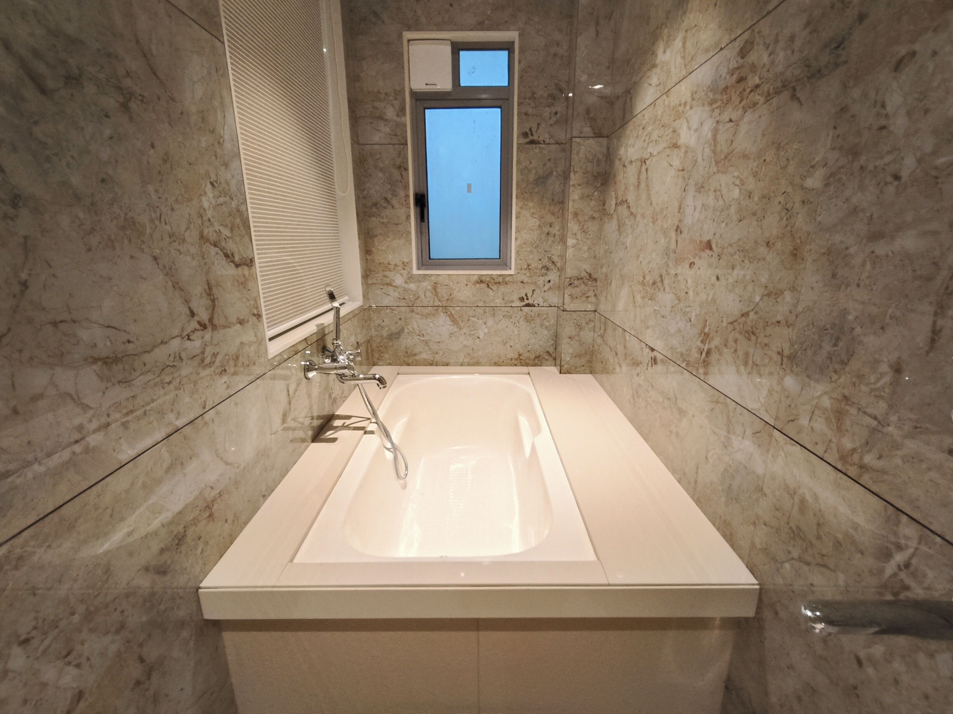 A bathroom with a large bathtub, a window, and marble walls.