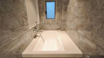 A bathroom with a large bathtub, a window, and marble walls.