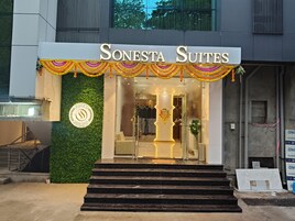 La entrada de Sonesta Suites con un diseño moderno, que incluye una escalera que conduce a la entrada, un logotipo en la pared y un letrero sobre la puerta.