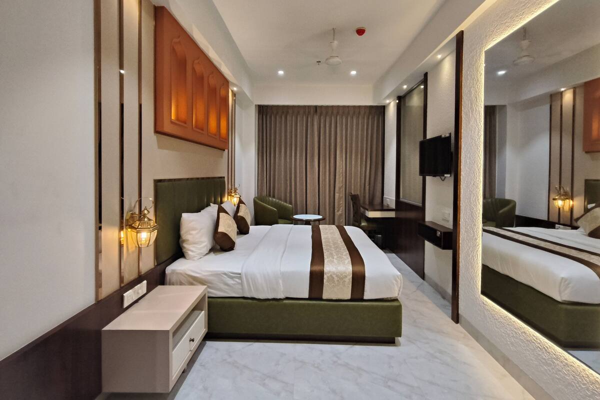 Una habitación de hotel moderna con una cama grande, un escritorio, una silla, un televisor y un espejo amplio.