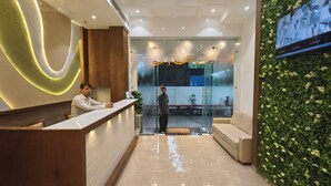 Zona de recepció amb un disseny modern, que inclou una taulella de recepció, un espai d'estar i una paret amb un dibuix de fullatge verd.