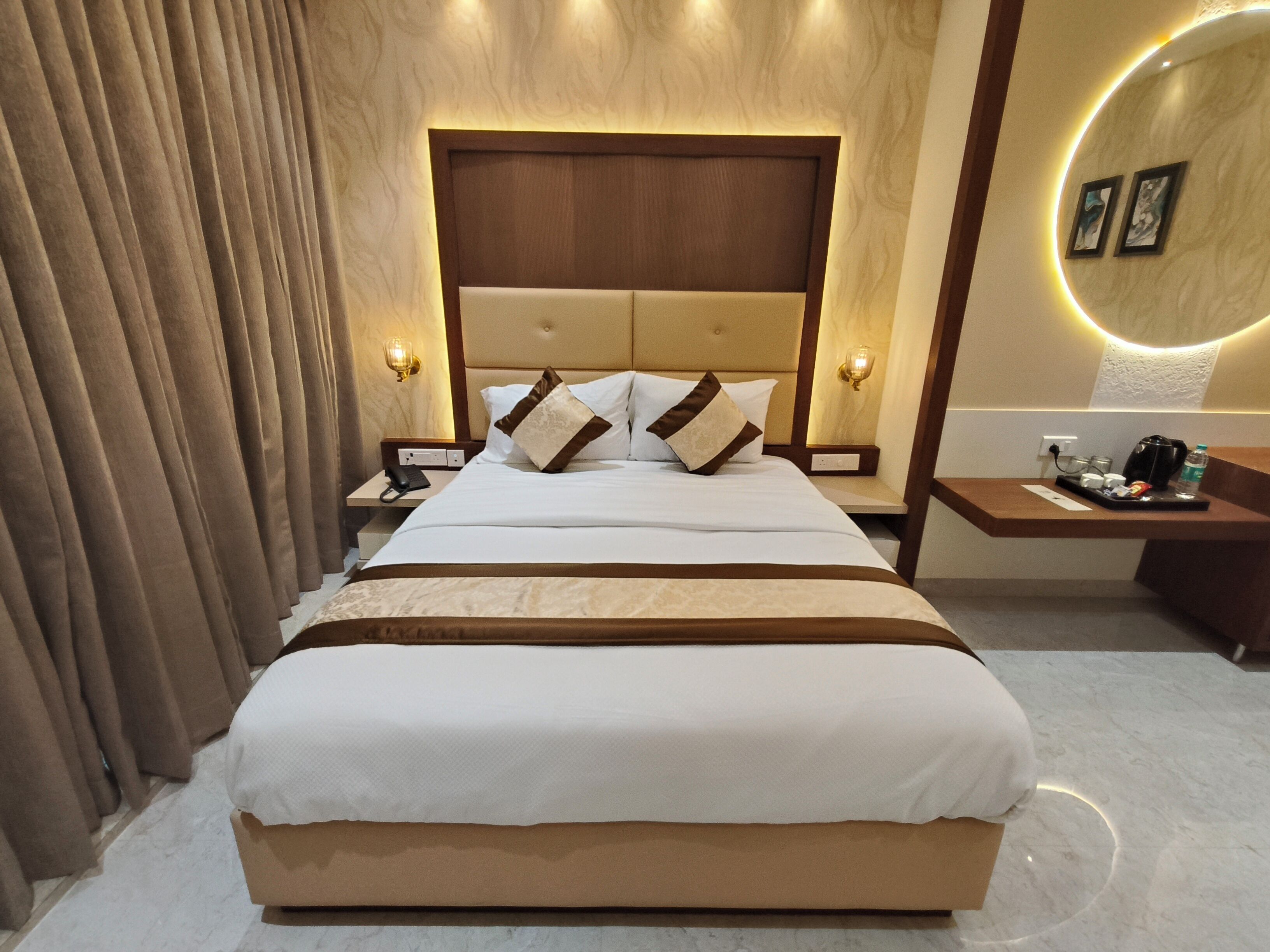 Habitación de hotel con una cama grande, una mesita de noche con lámpara y una pequeña mesa con una botella de agua y una bolsa.