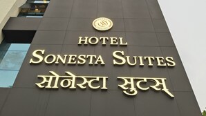 Edifici amb un cartell que diu "HOTEL Sonesta Suites" i inclou un logotip i algun text en un altre idioma.