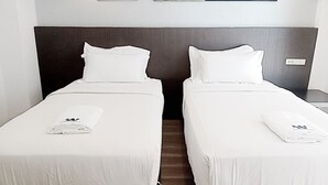 A hotel room with two single beds, each with a white bedspread and pillows, and a folded towel on each bed. - Whale Cha-Am (Cha-am)