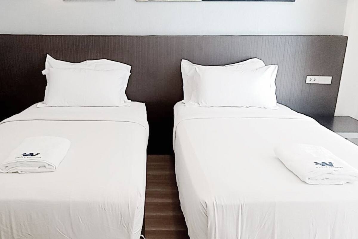 Ein Hotelzimmer mit zwei Einzelbetten, jeweils mit weißer Bettdecke und Kissen, und einem gefalteten Handtuch auf jedem Bett.