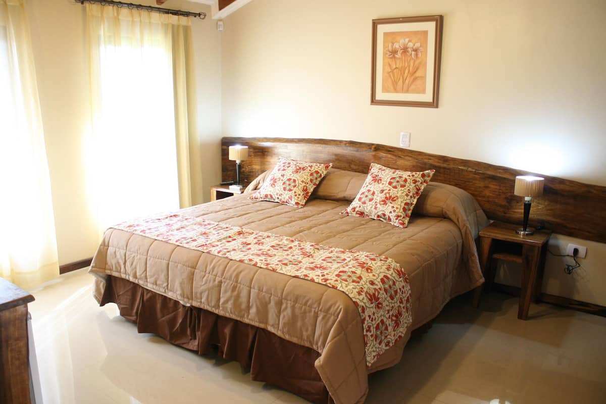 A neatly made bed with a brown bedspread and floral pillows, two bedside tables with lamps, and a framed picture on the wall.