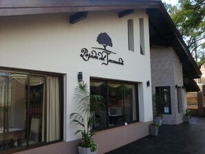 A building with a sign that reads 'Posada del Jardín.' There are large windows with curtains, potted plants, and a visible outdoor seating area. - Posada Del Jacarandá (Puerto Iguazú)