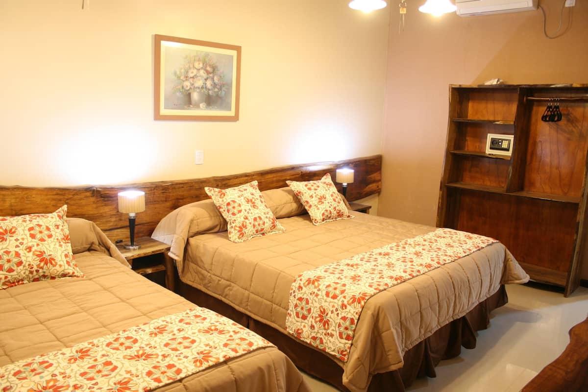 A hotel room with two beds, each with floral-patterned bedding and headboards. There is a wooden cabinet with a small radio and a framed floral painting on the wall.