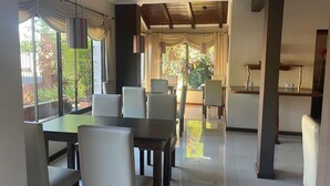 A dining area with tables and chairs, large windows, and a view of greenery outside. - Posada Del Jacarandá (Puerto Iguazú)