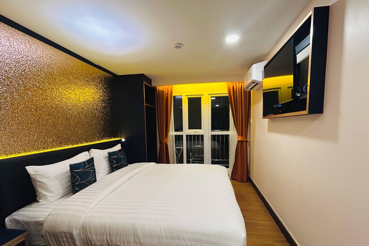 A modern hotel room with a large bed, a wall-mounted TV, and a window with curtains.