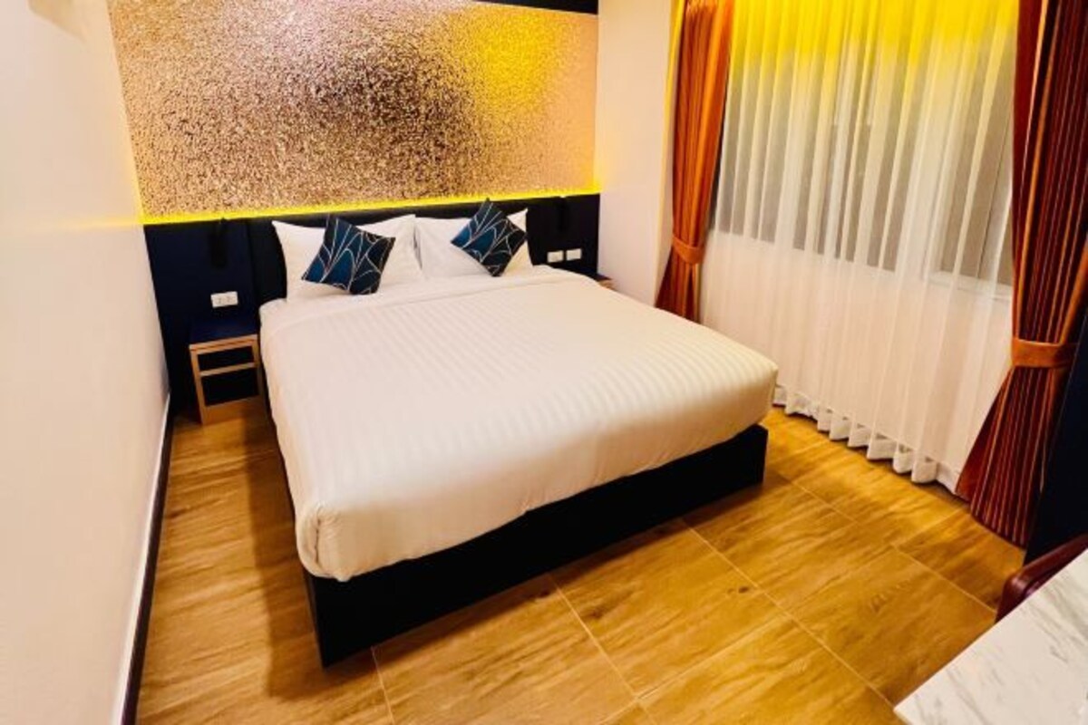 Uma cama bem arrumada com edredom branco e almofadas azuis e brancas, uma cabeceira de madeira e uma grande obra de arte abstrata na parede acima.
