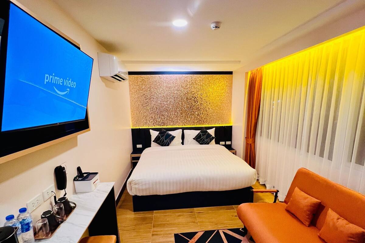 A hotel room with a bed, a desk with a computer, a TV displaying 'prime video', and a sofa.