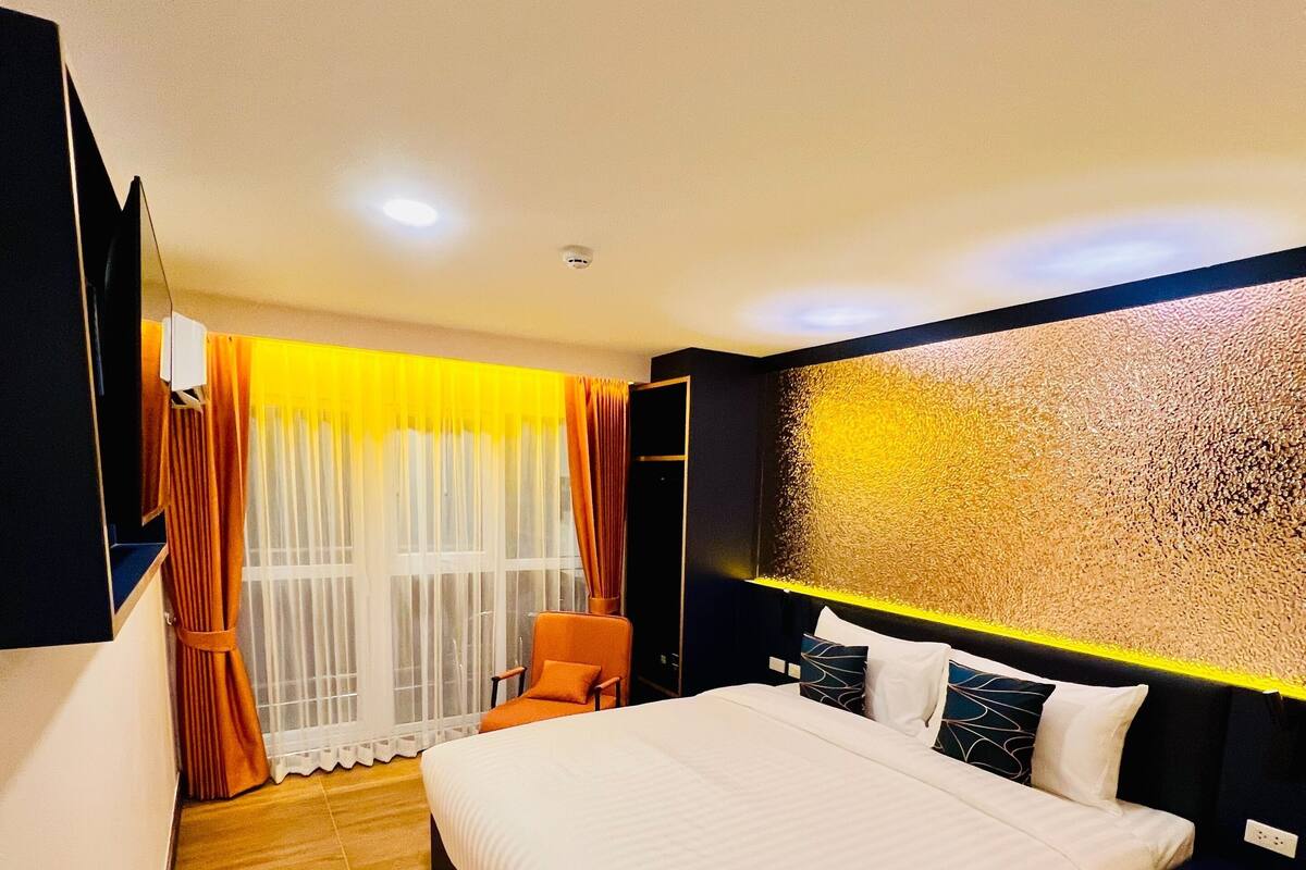 A modern hotel room with a large bed, a chair, a desk, and a TV.