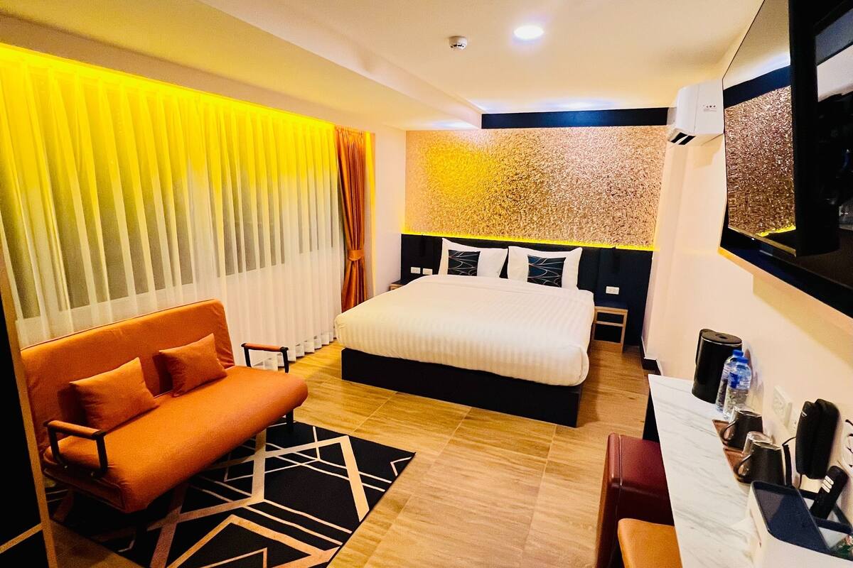 A modern hotel room with a large bed, a sofa, a desk, and a bathroom.