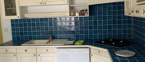 Une cuisine avec des meubles blancs, un lave-vaisselle, une cuisinière et un dosseret de carrelage bleu.