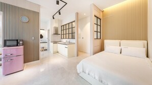 Un dormitorio moderno con una cama grande, una kitchenette y un electrodoméstico rosa.