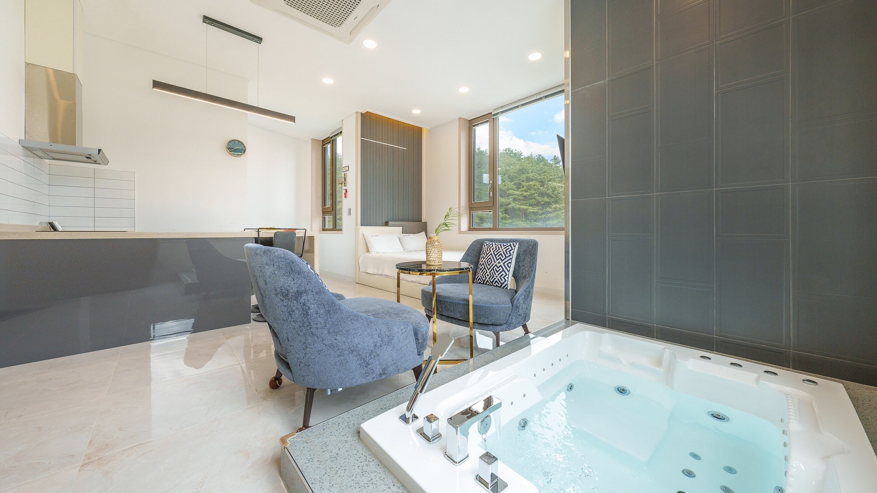 A modern bathroom with a large bathtub, a seating area with two chairs, and a large window offering a view of the outdoors.