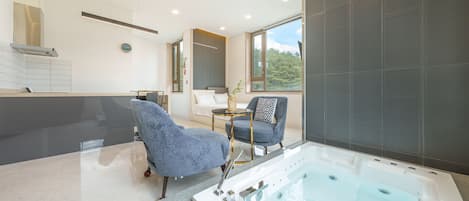 A modern bathroom with a large bathtub, a seating area with two chairs, and a large window offering a view of the outdoors.