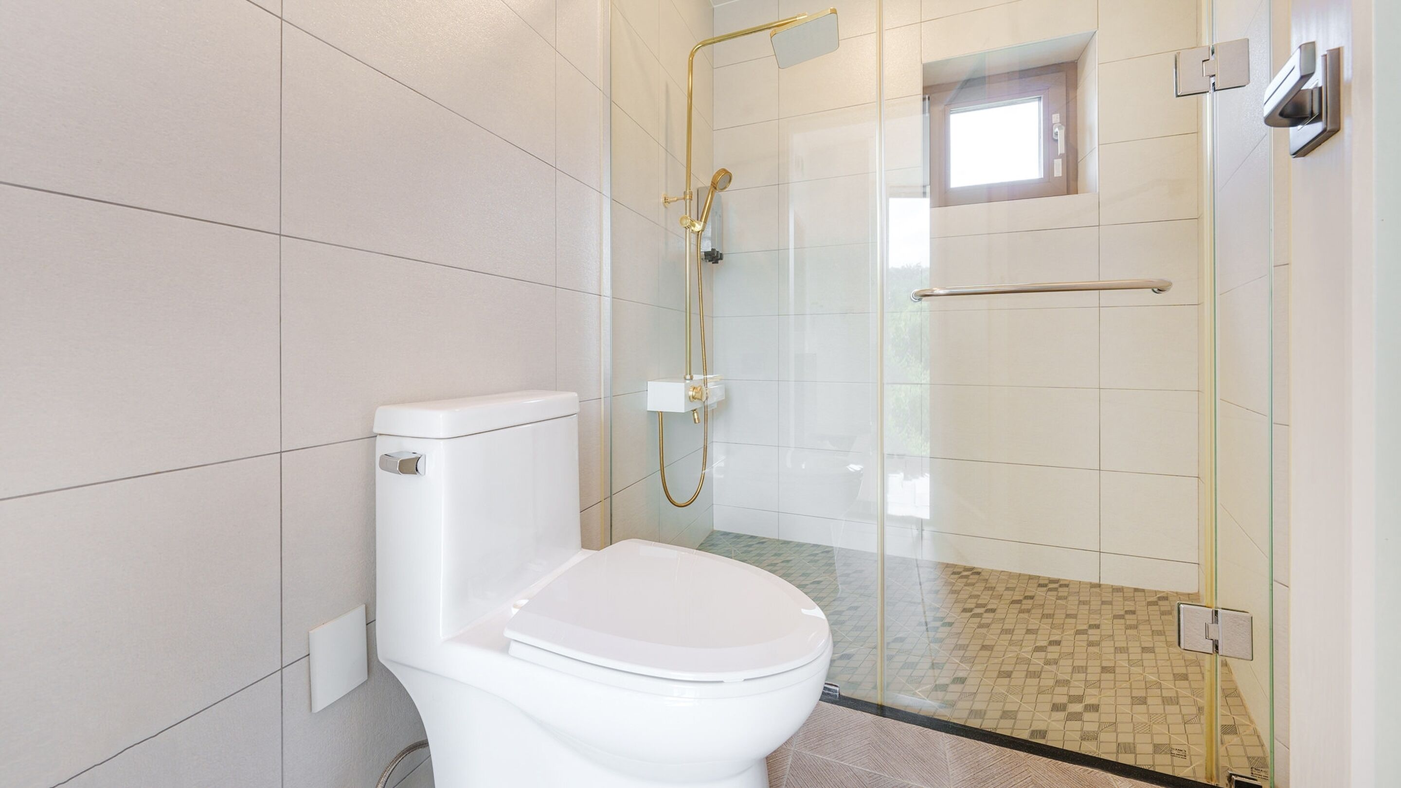 Ein modernes Badezimmer mit Toilette, einer begehbaren Glasdusche und einem kleinen Fenster.