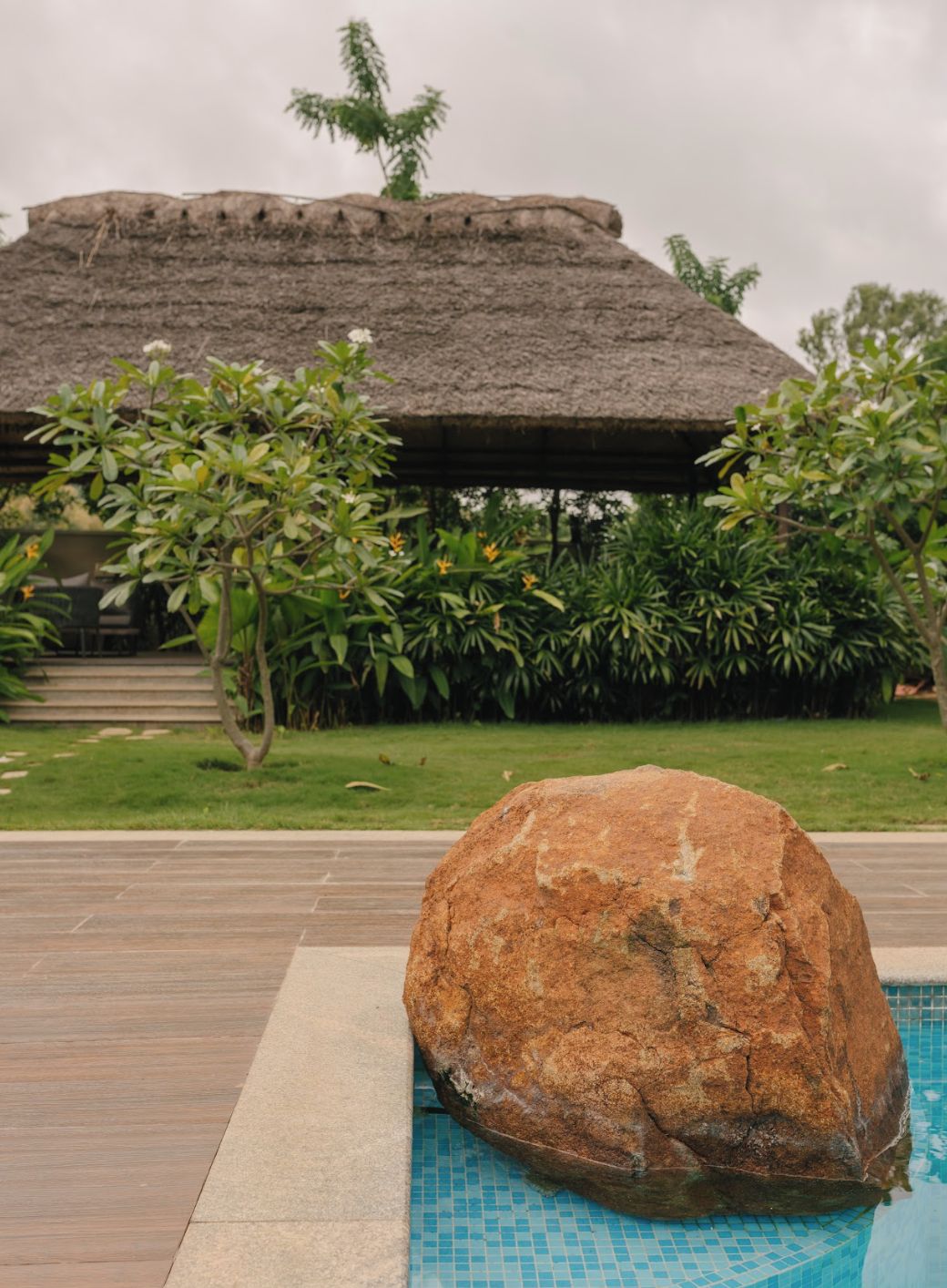 Un grand rocher dans un espace piscine, avec une structure à toit de chaume en arrière-plan.