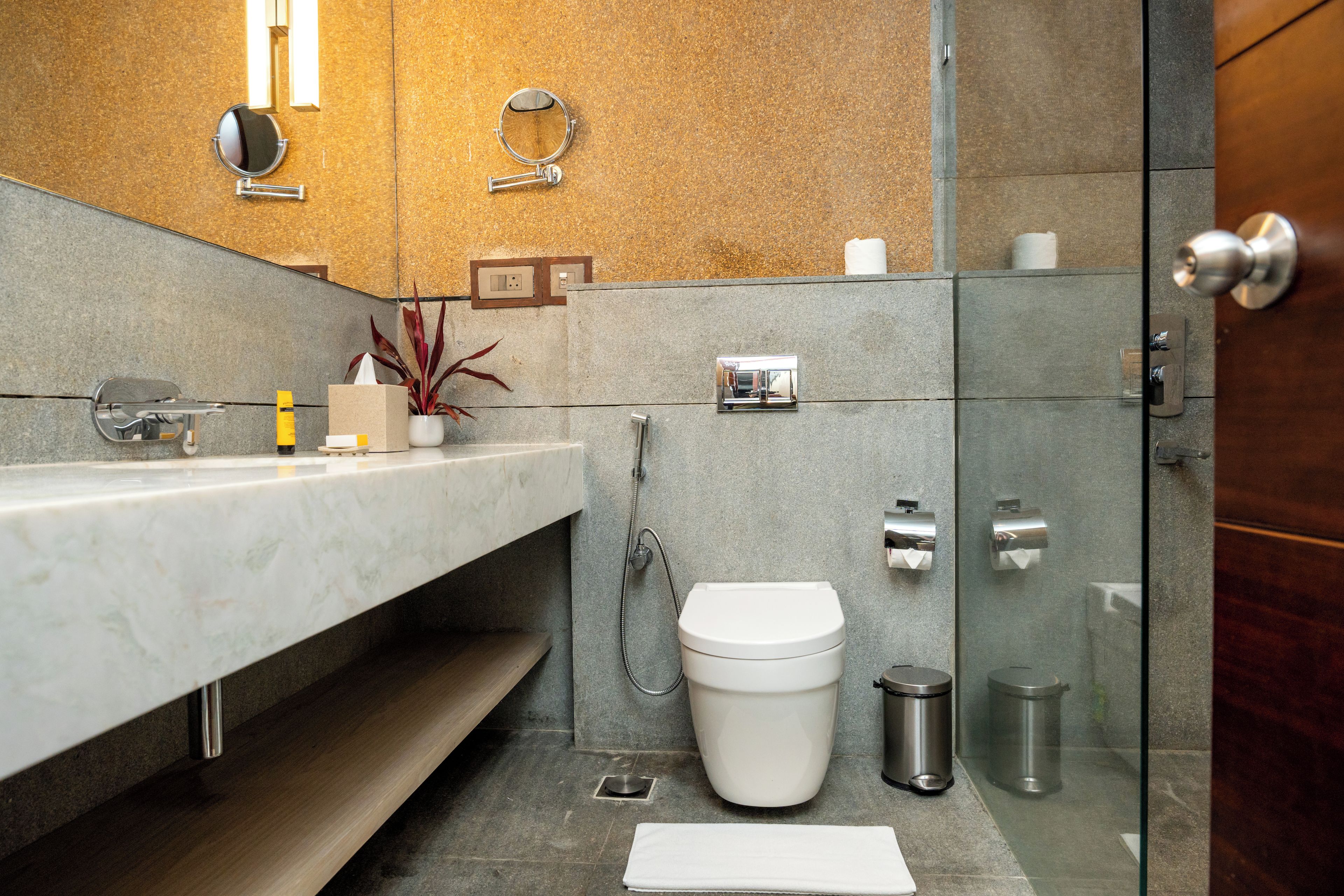 Een moderne badkamer met een marmeren wastafel, toilet, douche en een douchecabine met glazen wanden.